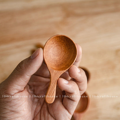 Hand holding a wooden spice spoon to show its size and shaped