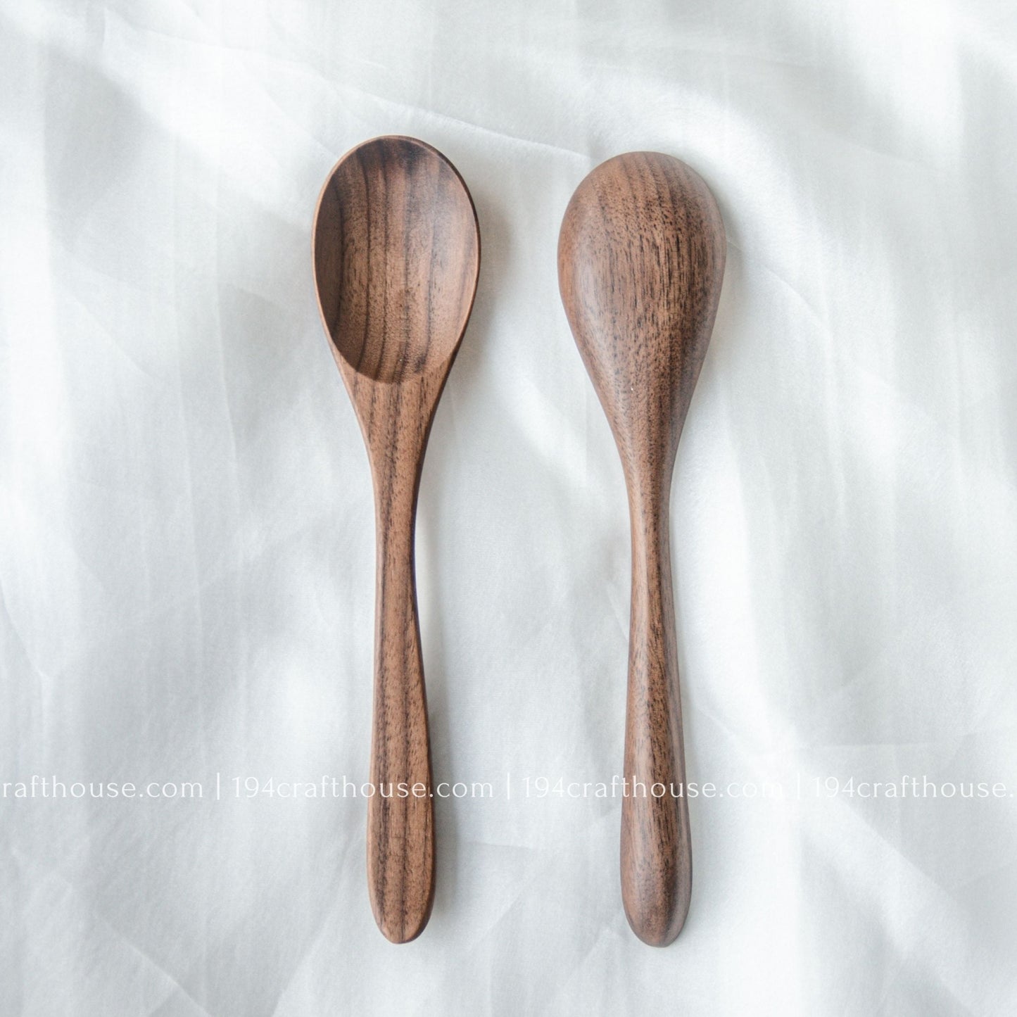 Set of two handcrafted 7-inch walnut wooden spoons displayed from the front on a light fabric background