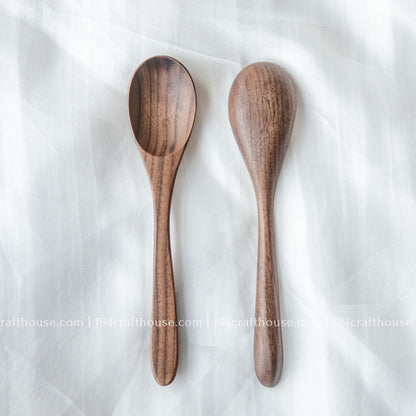 Set of two handcrafted 7-inch walnut wooden spoons displayed from the front on a light fabric background