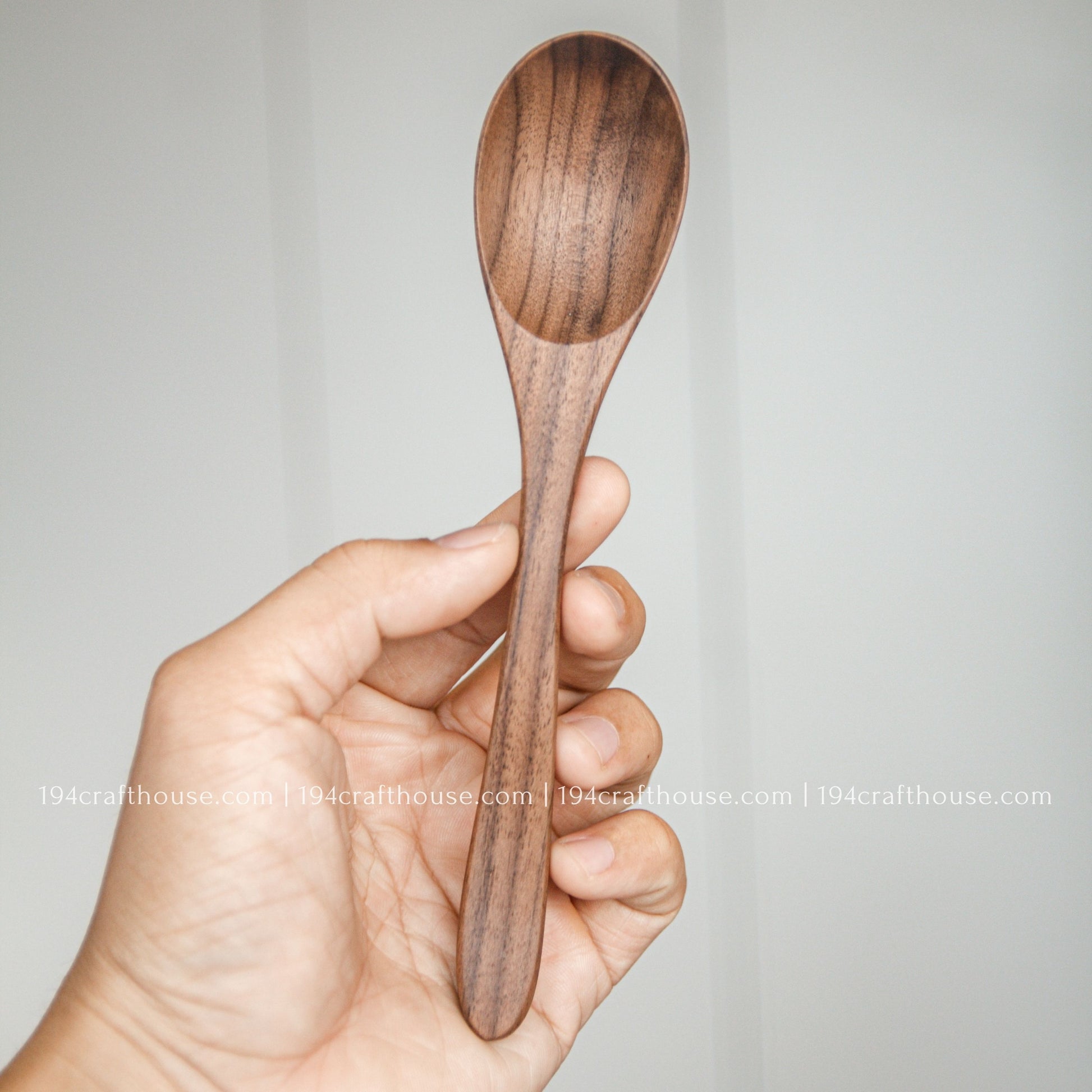 7-inch walnut wooden spoon held in hand to show its size, rounded bowl, and natural dark wood grain