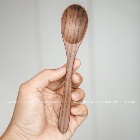 7-inch walnut wooden spoon held in hand to show its size, rounded bowl, and natural dark wood grain
