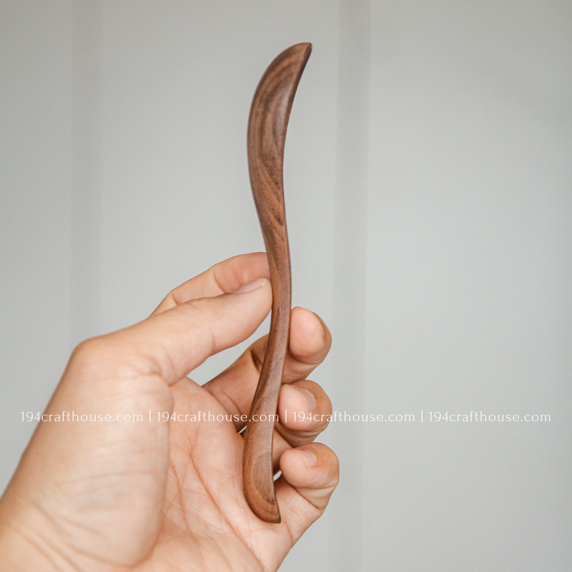 Side view of a 7-inch walnut wooden spoon held in hand to show its slim profile and handcrafted shape