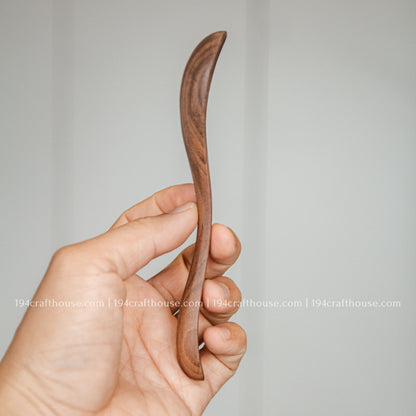 Side view of a 7-inch walnut wooden spoon held in hand to show its slim profile and handcrafted shape