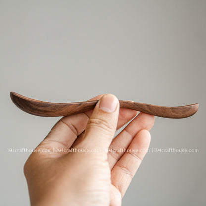 Side view of a handcrafted 6-inch walnut wooden spoon held in hand to show its slim profile and smooth finish