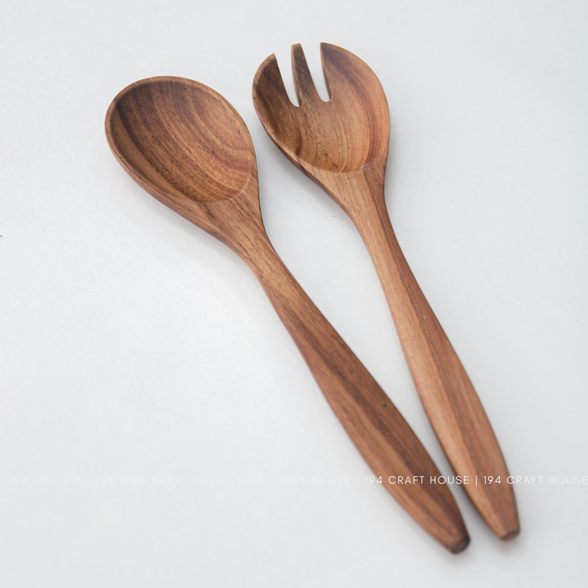 Acacia wood salad servers lying at an angle, spoon bowl and fork slots in natural brown wood