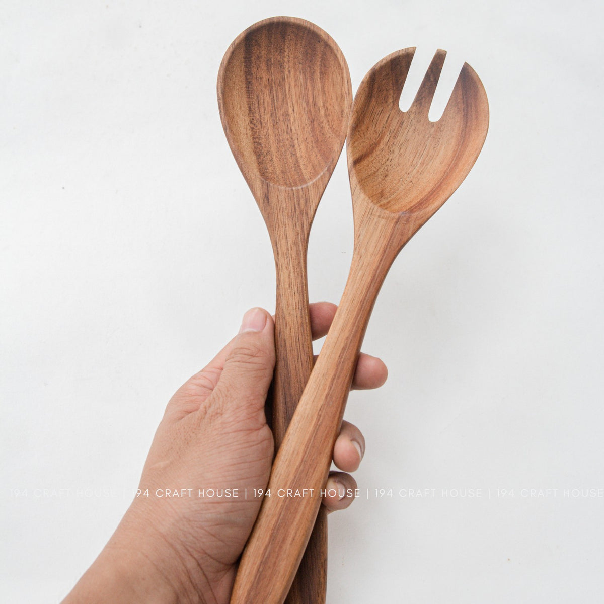 Hand holding acacia wood salad spoon and fork to show handle size and grip