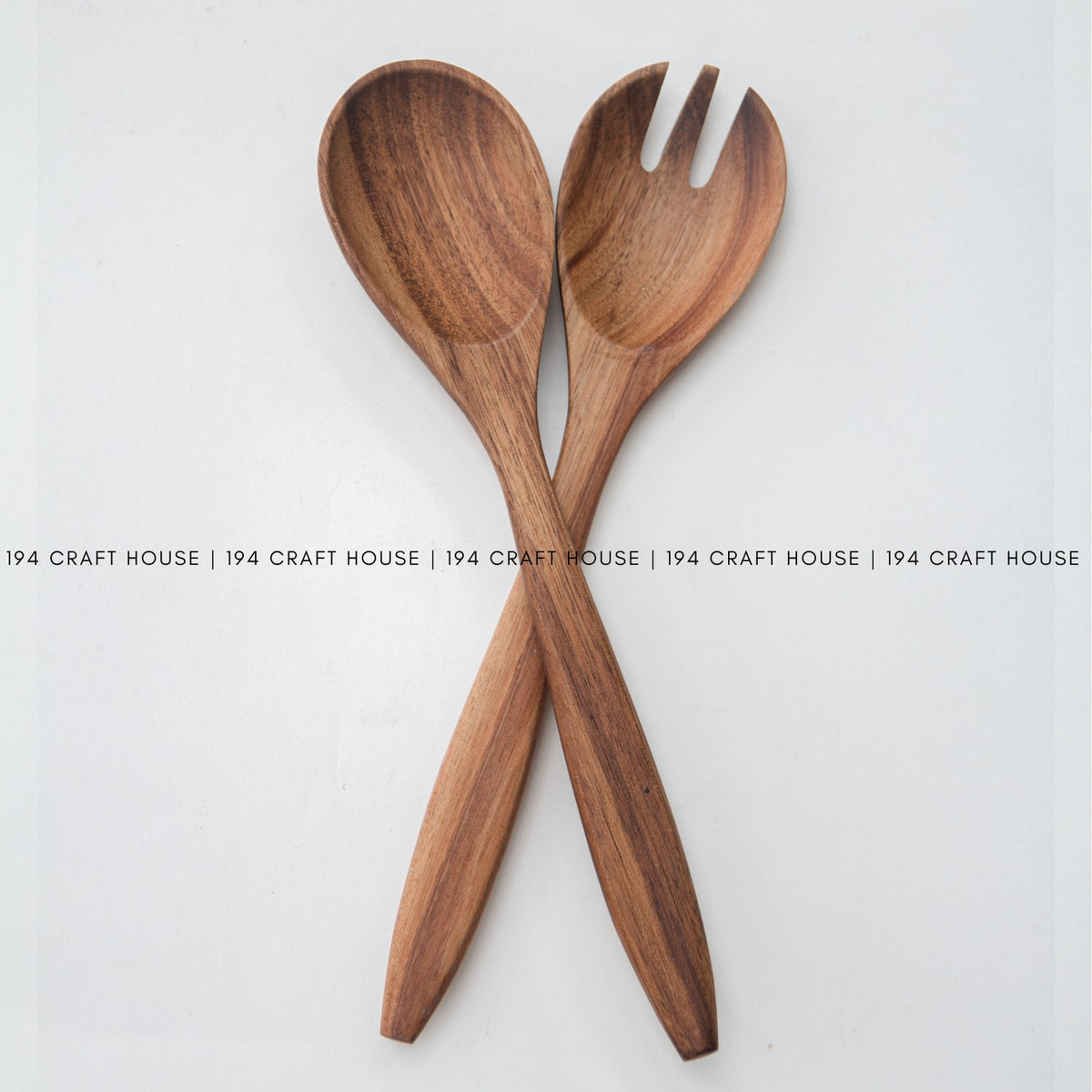 Acacia wood salad spoon and fork crossed on a white background, warm brown grain