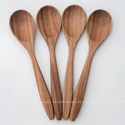 Four acacia wood salad spoons laid side by side with tapered handles on white