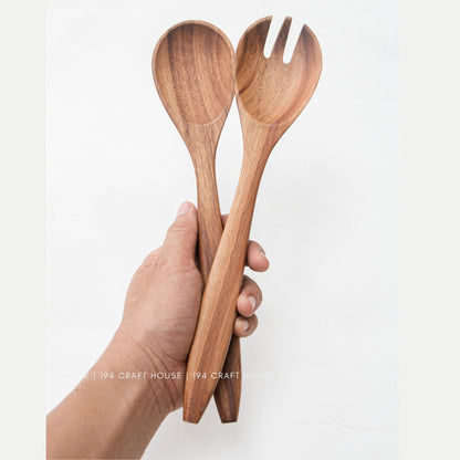 Hand holding wooden salad servers upright, acacia spoon and slotted fork heads on top