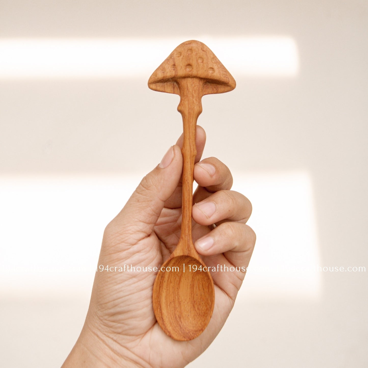 Hand-carved mushroom wooden spoon crafted from doussie wood, featuring a sculpted mushroom cap handle hold by hand on a white background.