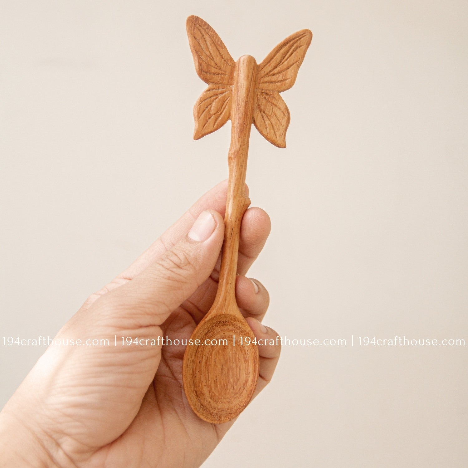 Hand-carved Butterfly wooden spoon crafted from doussie wood, featuring a sculpted butterfly handle hod by on a white background.and 