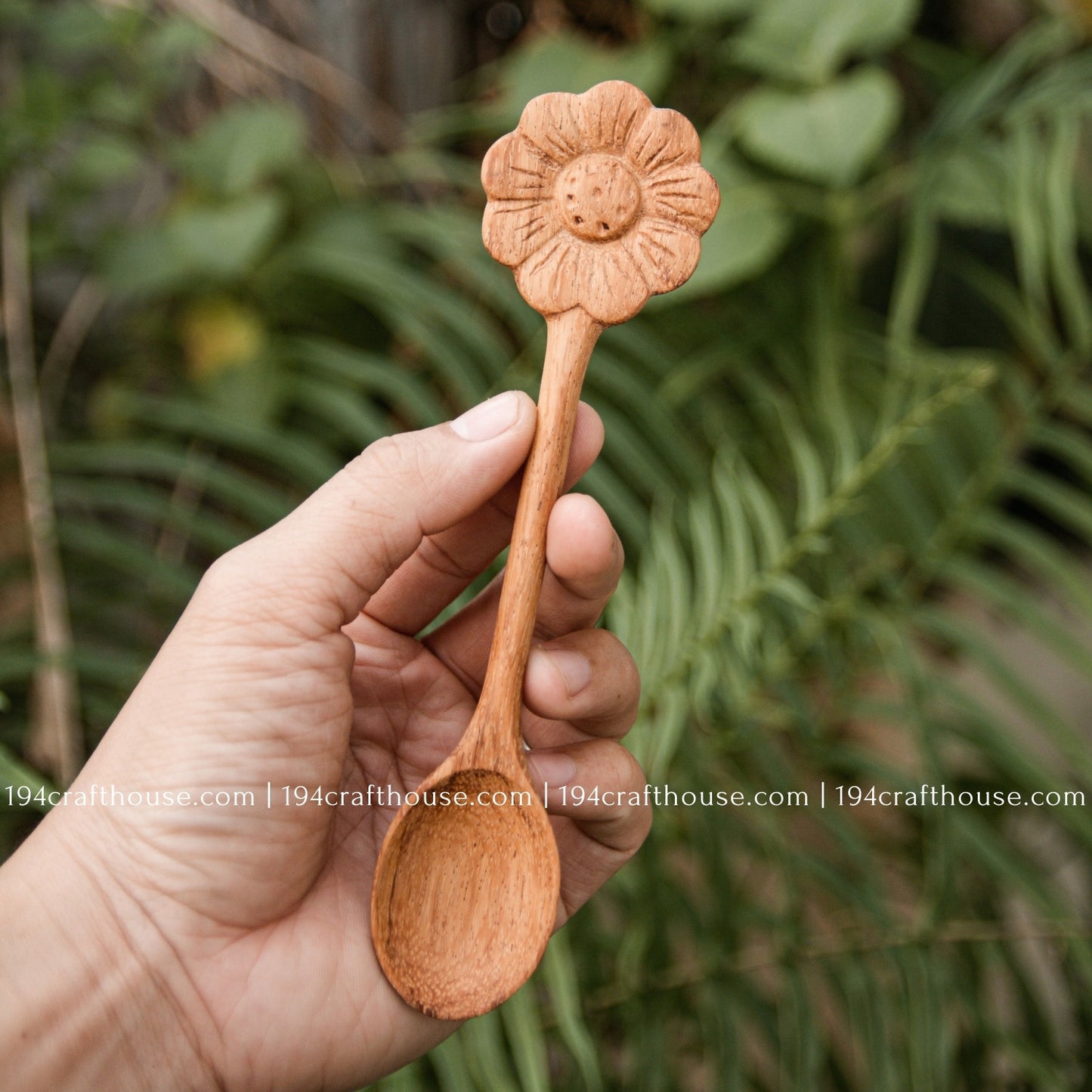 Hand-carved Flower wooden spoons crafted from doussie wood, featuring a sculpted flower handle hold by hand on a green tree background