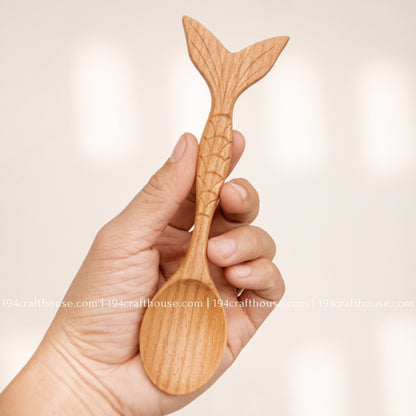 Reverse view of the Doussie wood spoon held in hand, highlighting the carved fish-tail end and natural grain.