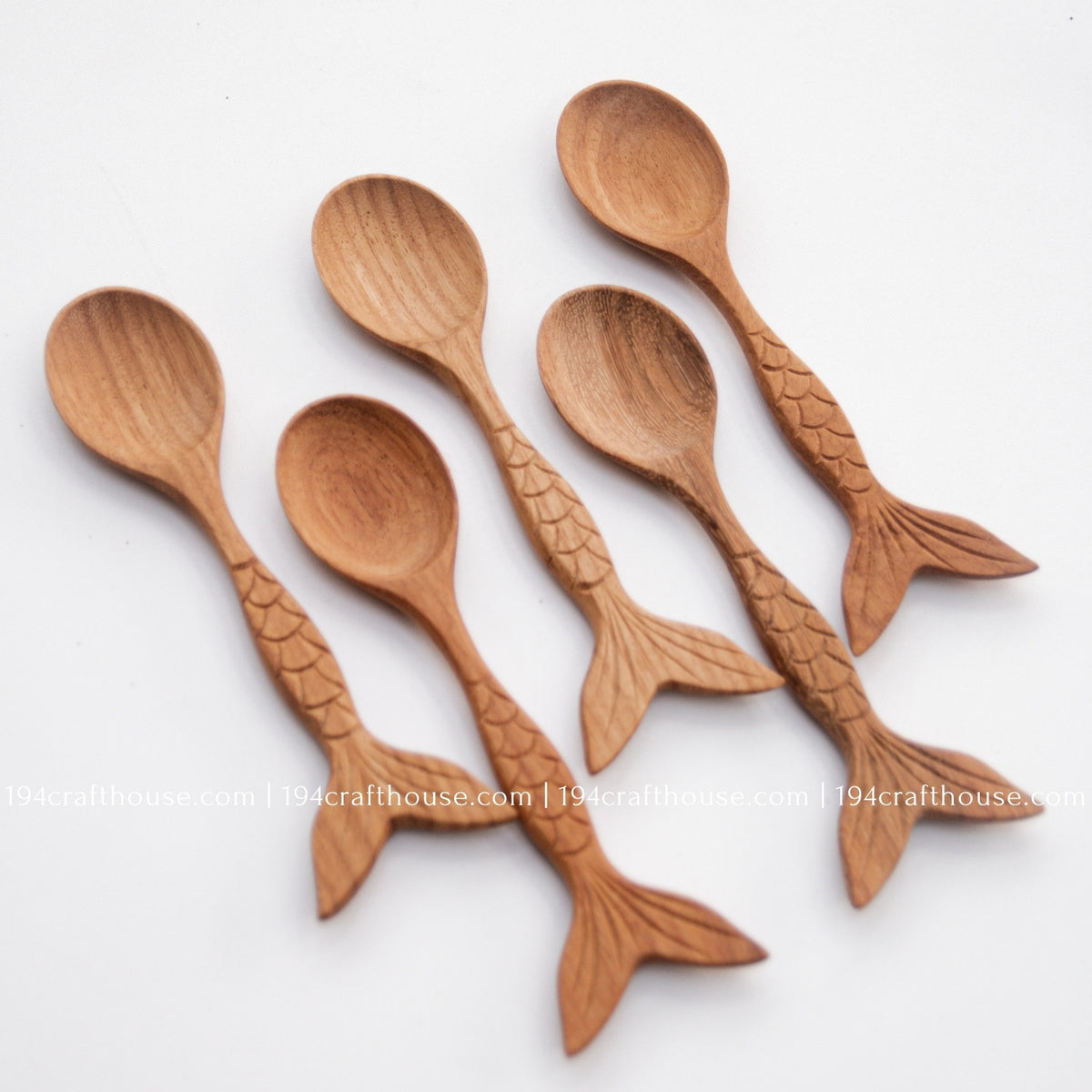 Fish-tail handle Doussie wood spoons arranged on a pale background to display shape and grain variation.