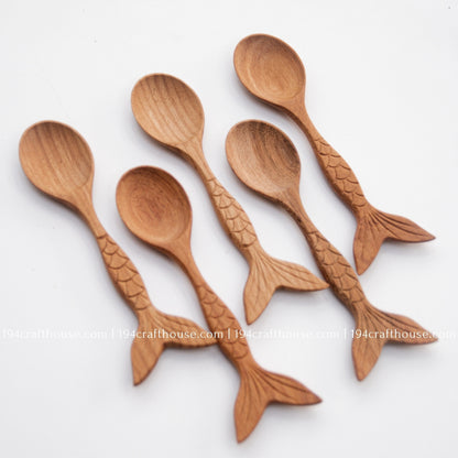 Fish-tail handle Doussie wood spoons arranged on a pale background to display shape and grain variation.