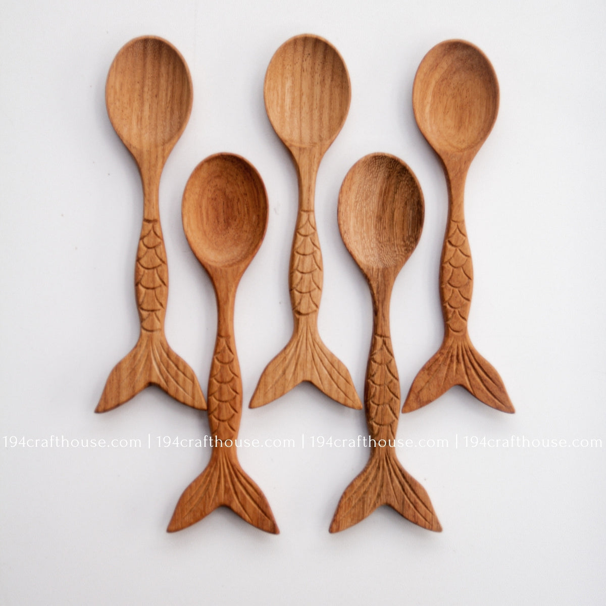 Five handcrafted Doussie wood spoons arranged together, showing oval bowls and fish-tail handles.