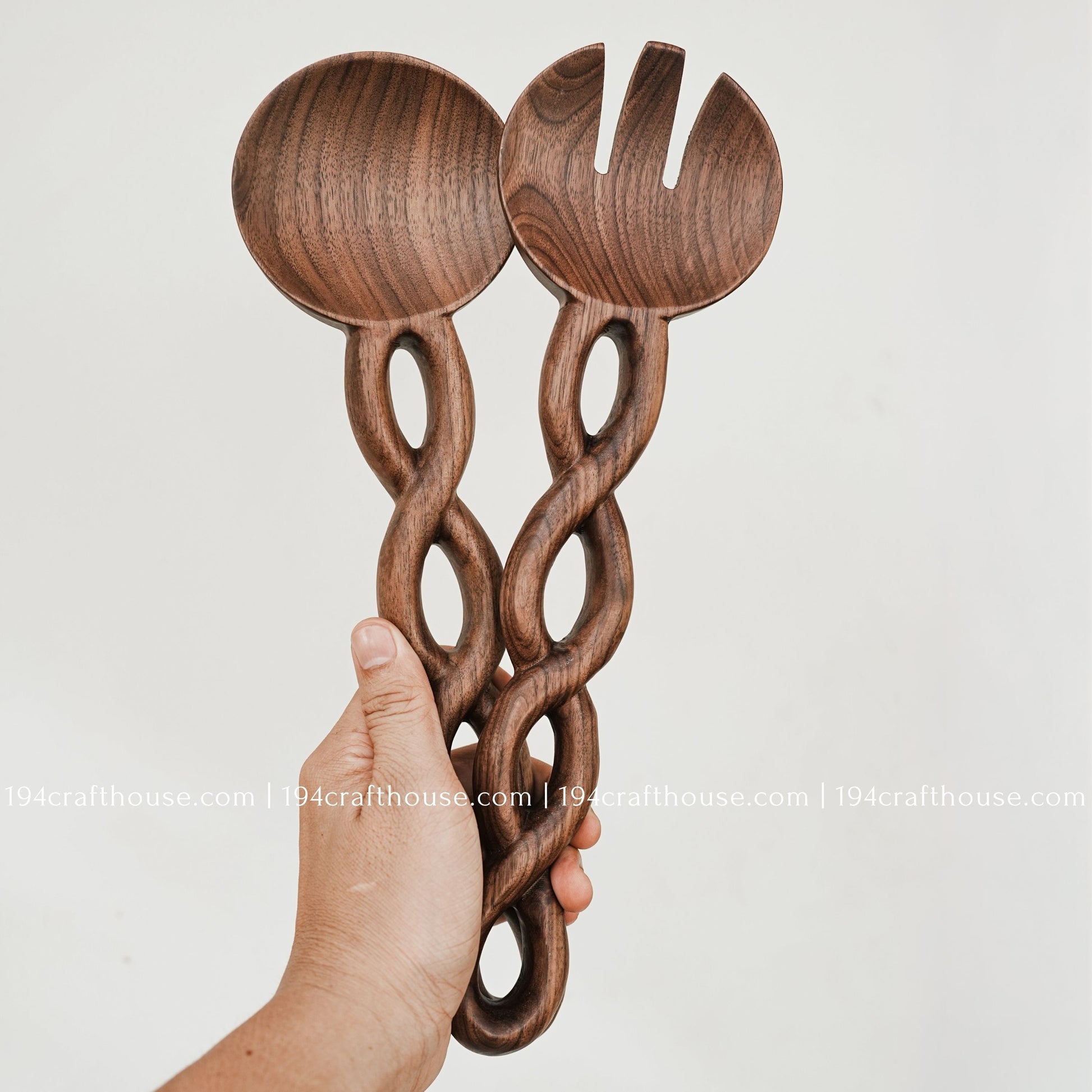 Wooden salad spoon and fork held in hand to show their size, carved chain handles, and craftsmanship