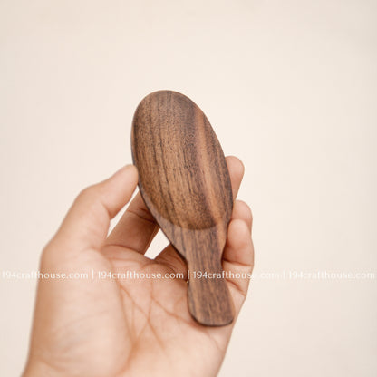 Hand holding a compact walnut wood tea scoop to show its short handle, scale and oval bowl.