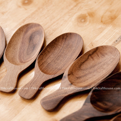 Several walnut wood tea scoops arranged on a wooden surface, displaying their compact short-handle design.