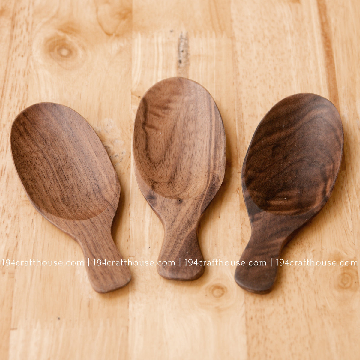 Three walnut wood tea scoops together, showing natural variation in grain, tone and bowl shape.