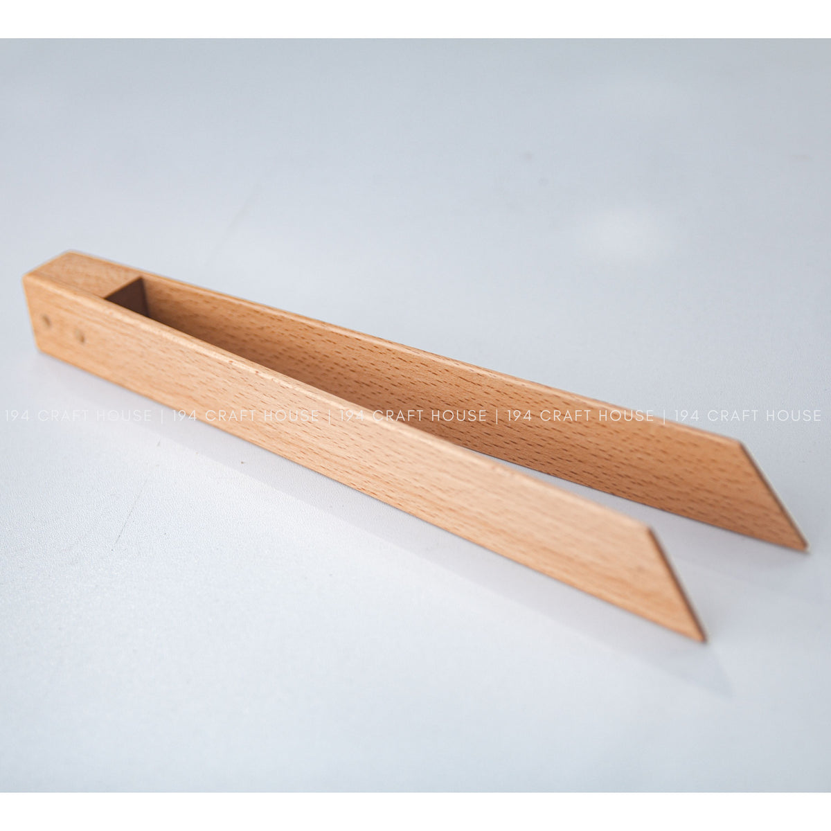 Open wooden salad tongs shown at an angle against a pale background.