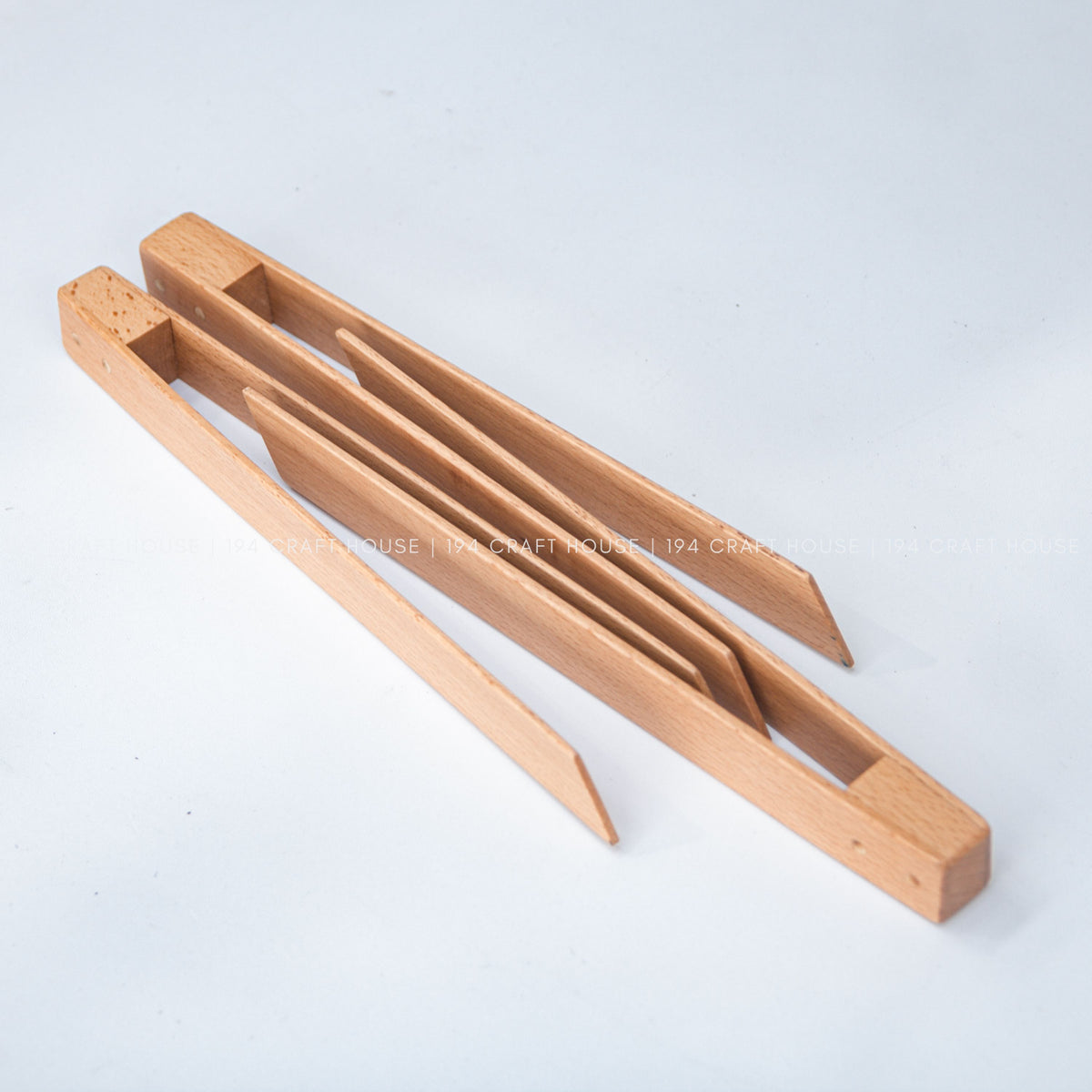 The open wooden salad tongs lie diagonally on a light surface, showing both long arms.