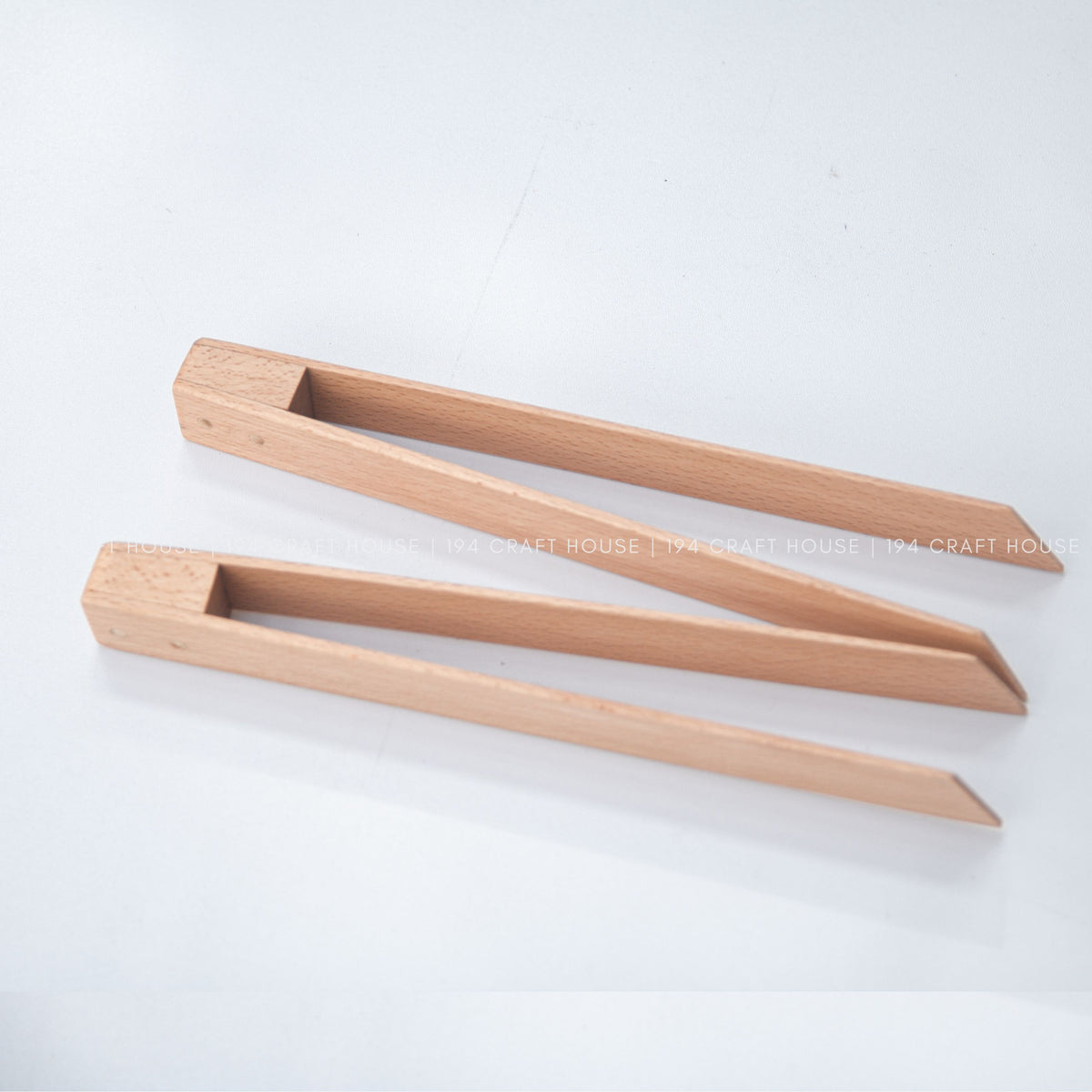 Two light wood salad tongs lie open and parallel on a pale surface.