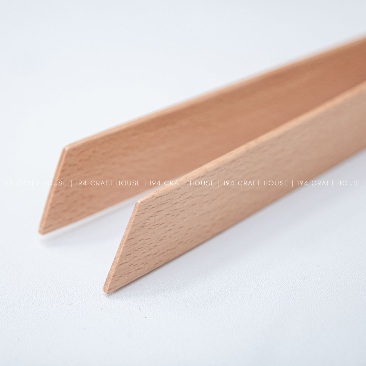 Close-up of the tapered ends of two light wood salad tongs against a pale background.