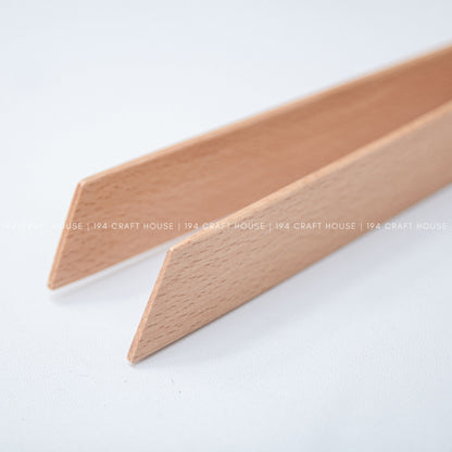 Close-up of the tapered ends of two light wood salad tongs against a pale background.