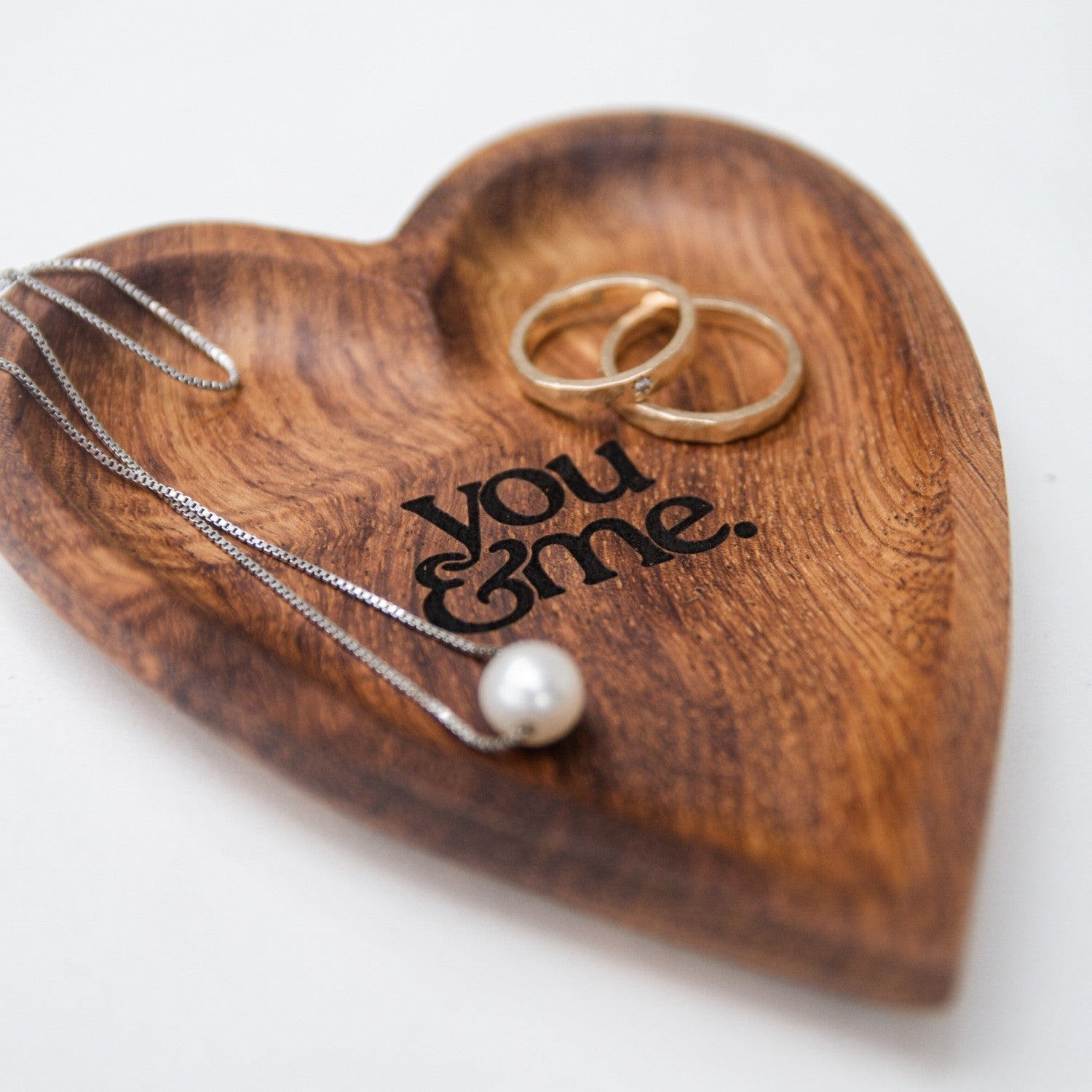 Wooden heart-shaped jewelry holder with 'you & me' engraving, holding a ring and necklace.