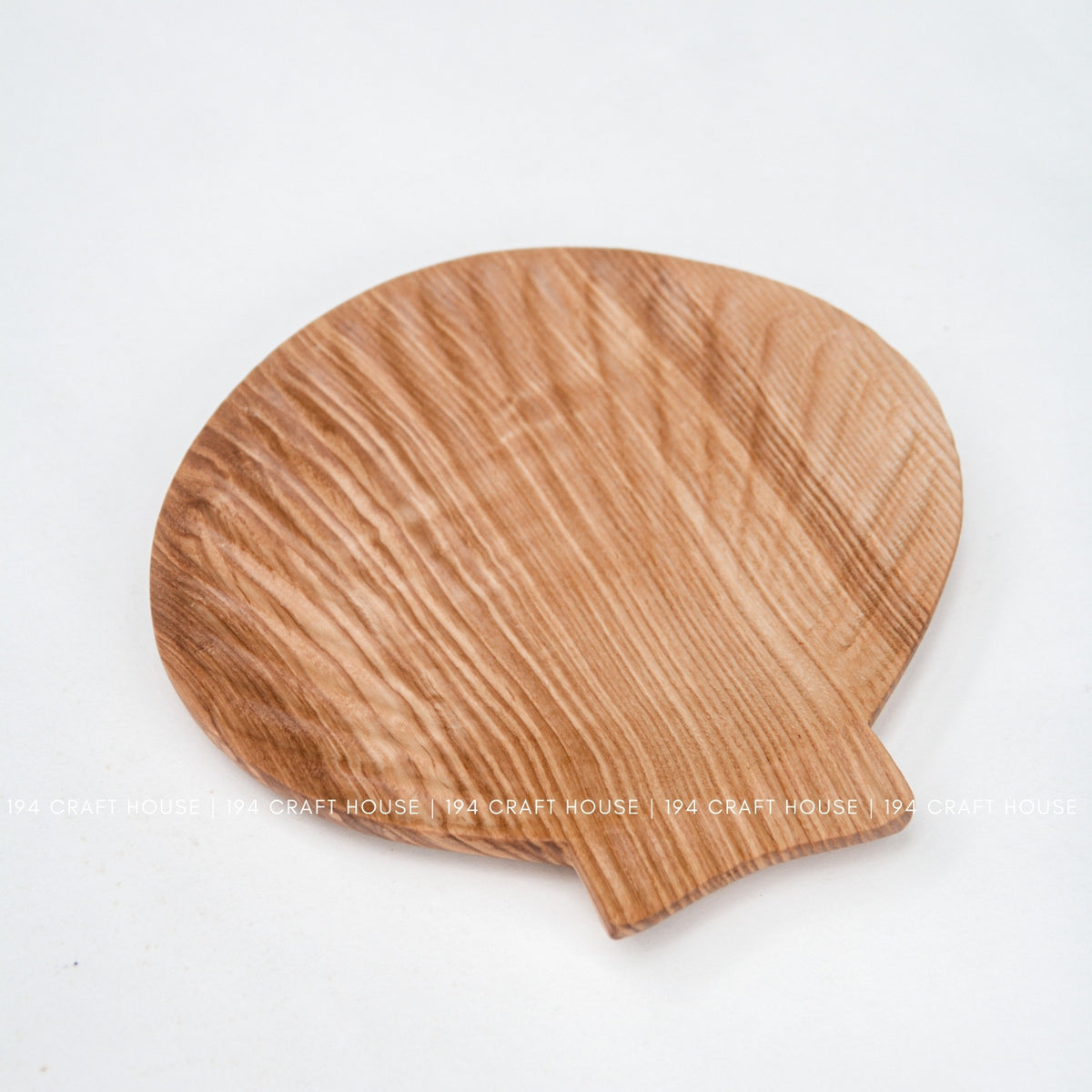 Angled view of the rounded ash wood tray showing its flowing grain and short projecting tab.