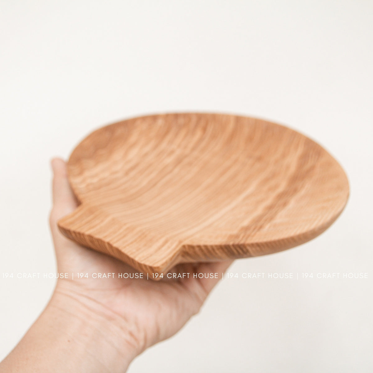 A hand supports the ash wood tray from below, showing its shallow profile and rounded edge.