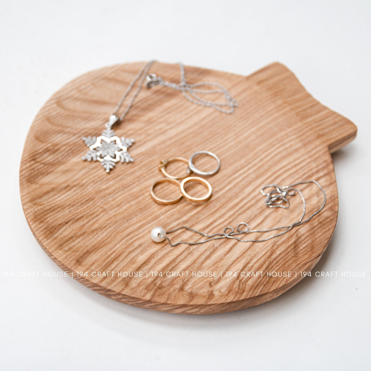 The ash wood tray displays rings and necklaces on its grain-patterned surface.