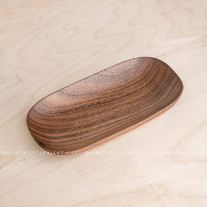 Single wooden oval tray at an angle showing darker grain patterns on warm brown wood