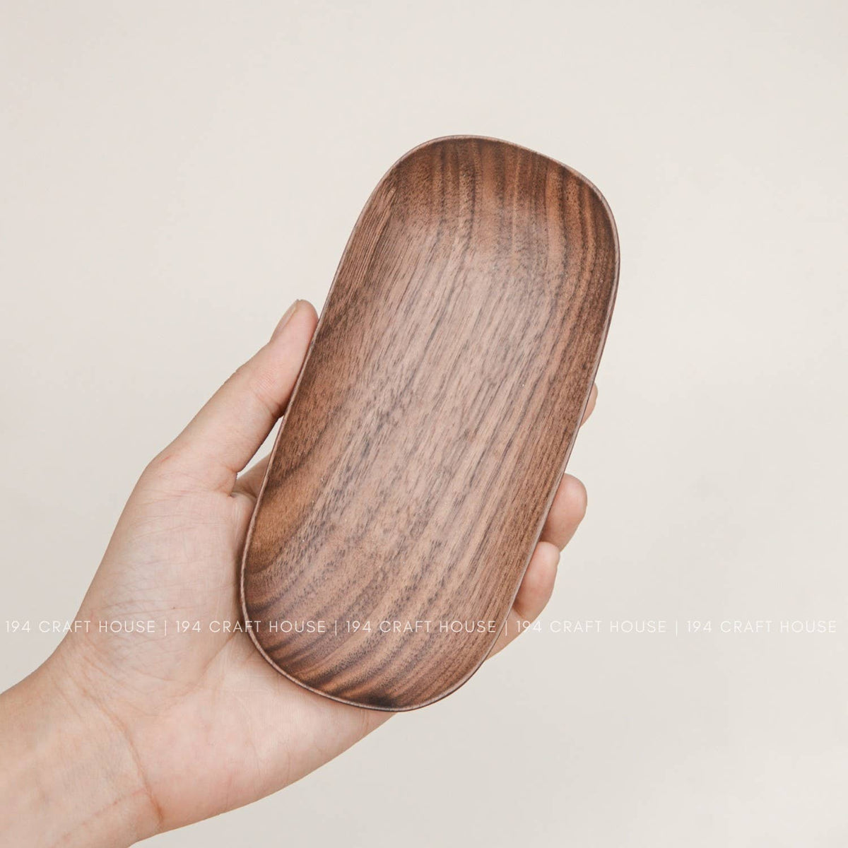 Hand holding a warm brown wooden oval tray with darker grain patterns to show its scale