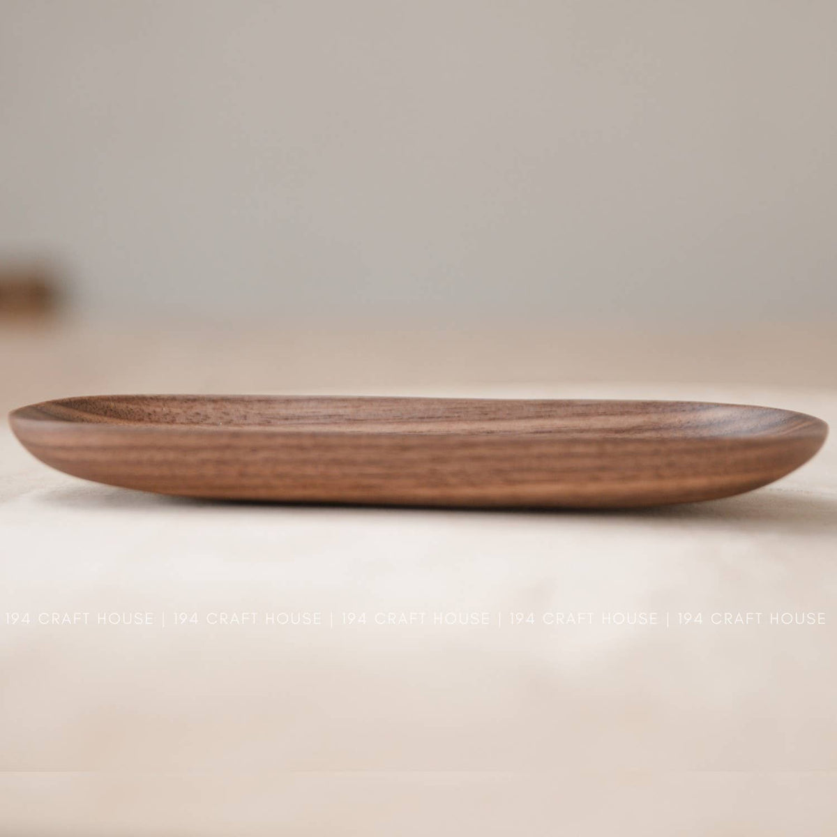Low side view of a shallow wooden oval tray with horizontal grain lines in warm brown wood