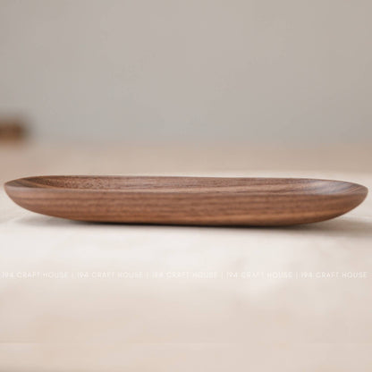 Low side view of a shallow wooden oval tray with horizontal grain lines in warm brown wood