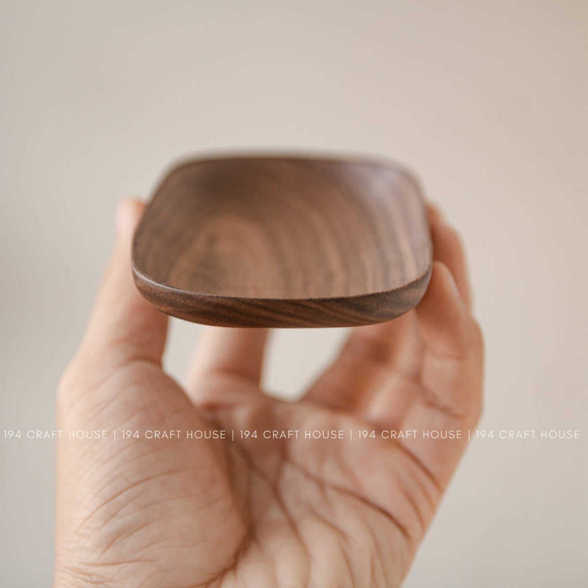 Wooden oval tray held in a hand showing its rounded rim and shallow warm brown interior