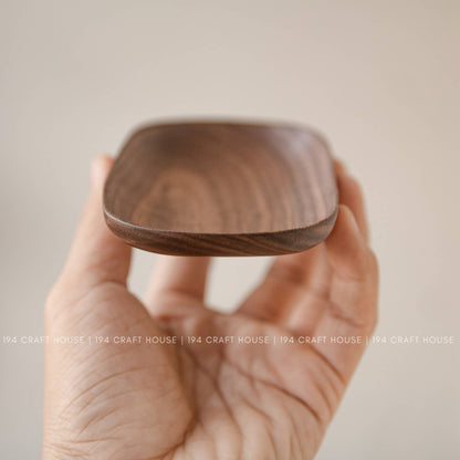 Wooden oval tray held in a hand showing its rounded rim and shallow warm brown interior