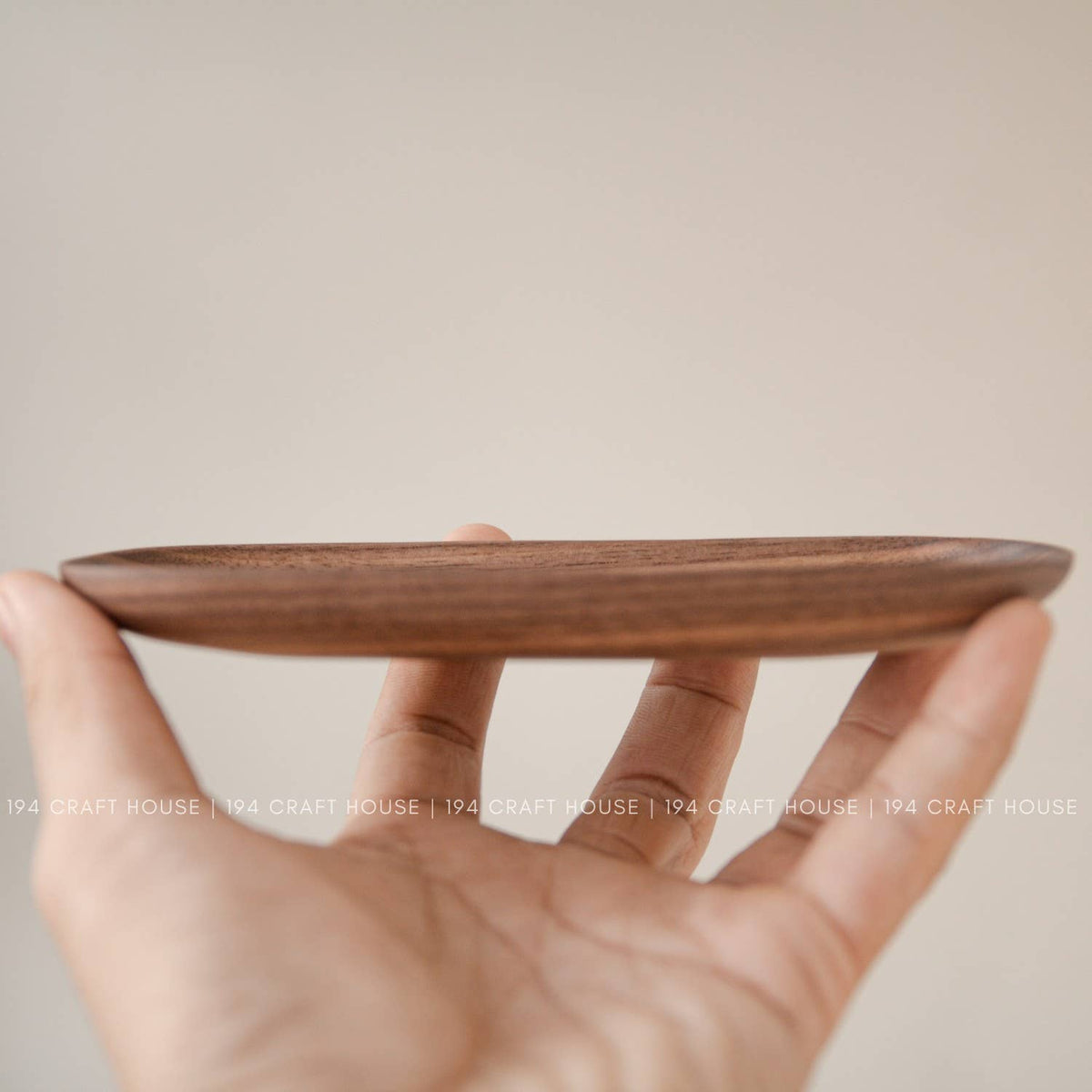 Side profile of a thin wooden oval tray balanced on fingertips, showing its shallow warm brown shape