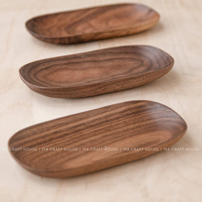 Three warm brown wooden oval trays with visible grain lined up on a light wood surface