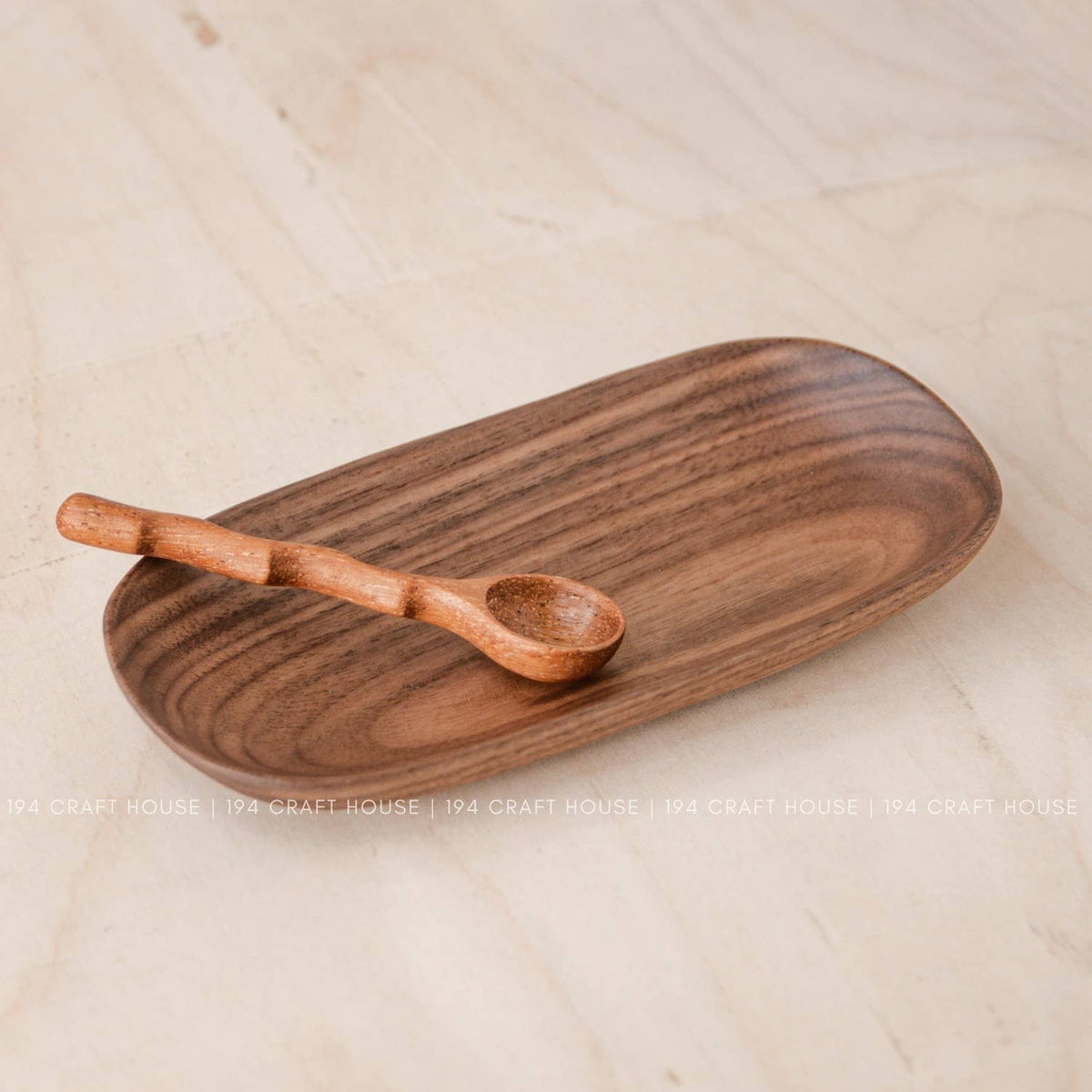 Wooden oval tray in warm brown with a small wooden spoon resting on it, on a light wood table