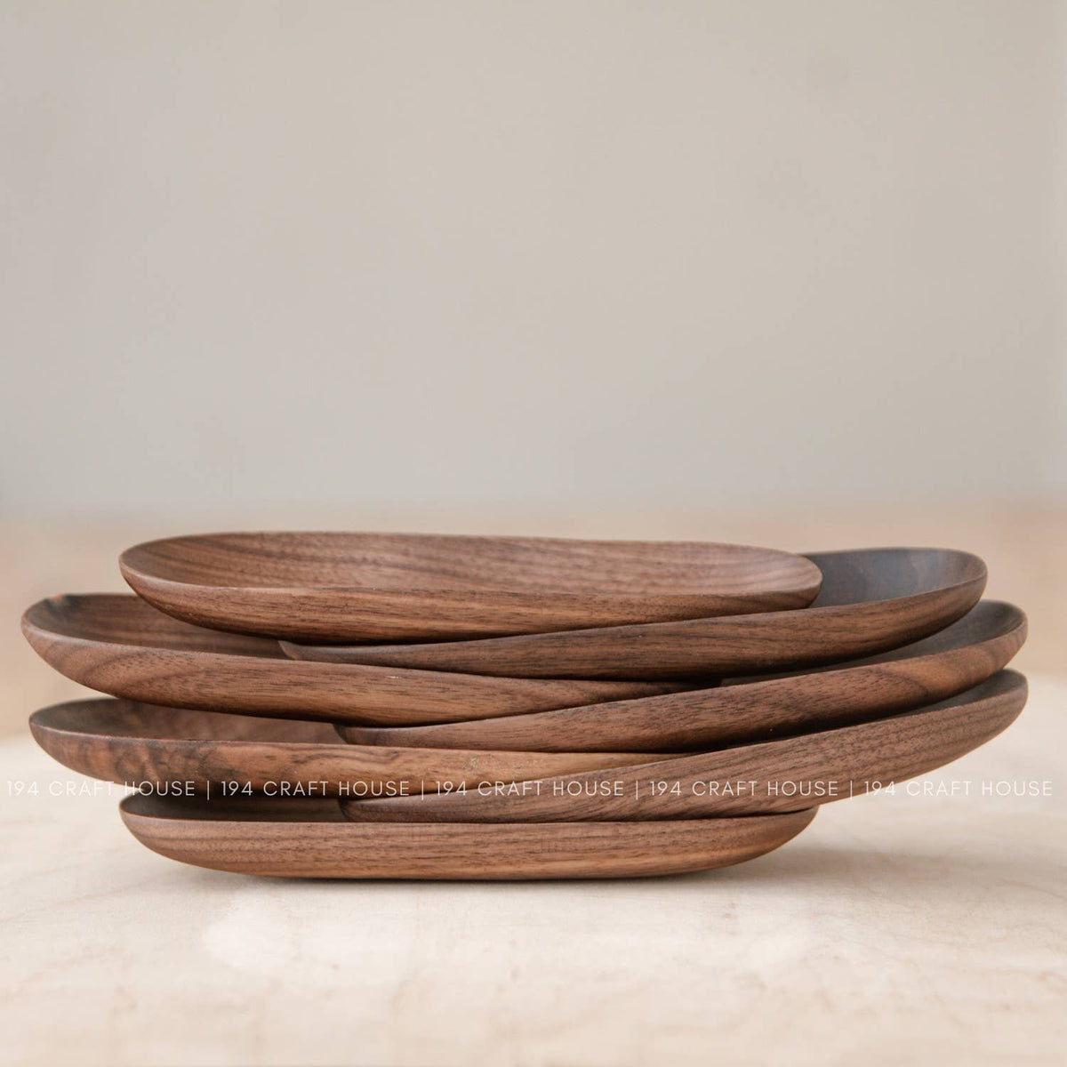 Stack of warm brown wooden oval trays seen from the side, showing the grain on the rims