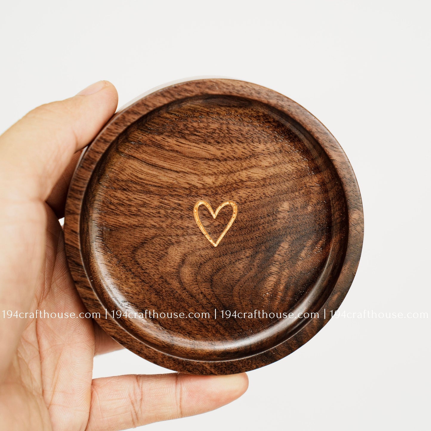 Walnut wood jewelry dish held in hand, showing the gold heart engraving, rounded shape, and natural wood grain