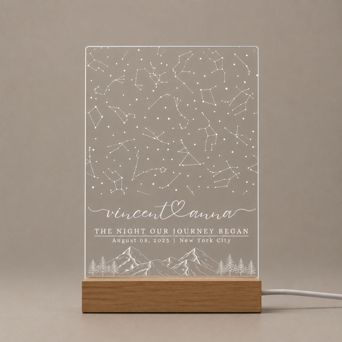 Studio front view of unlit clear acrylic plaque featuring full constellation star map engraving, couple names, and mountain art mounted on a natural beech wood base.