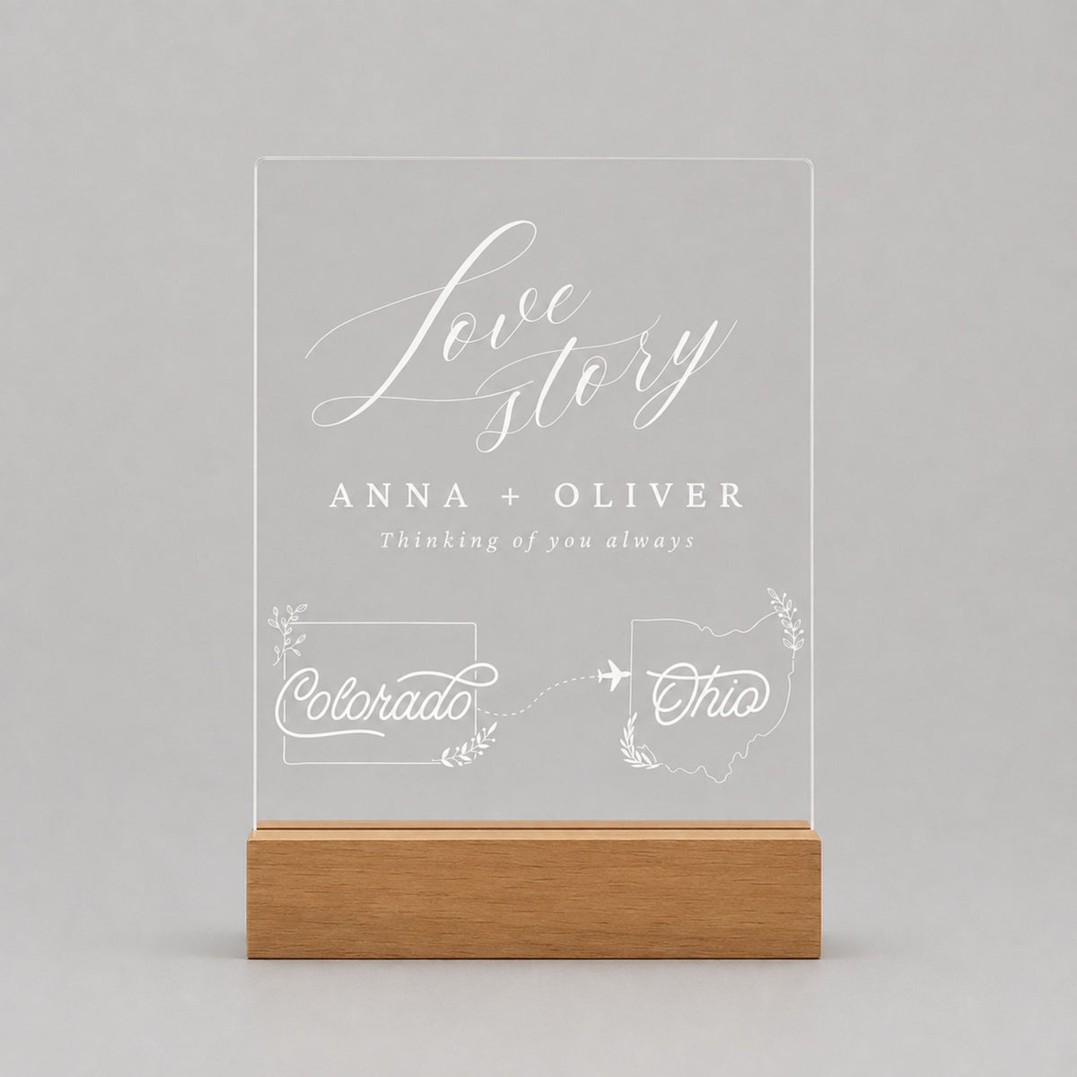Studio front view of unlit clear acrylic plaque laser-engraved with custom Colorado and Ohio state outlines, flight path, and couple names in a solid wood base.