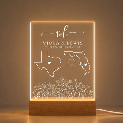 Studio front view of illuminated floral long distance state map acrylic night light glowing warm white on a natural wooden LED base.