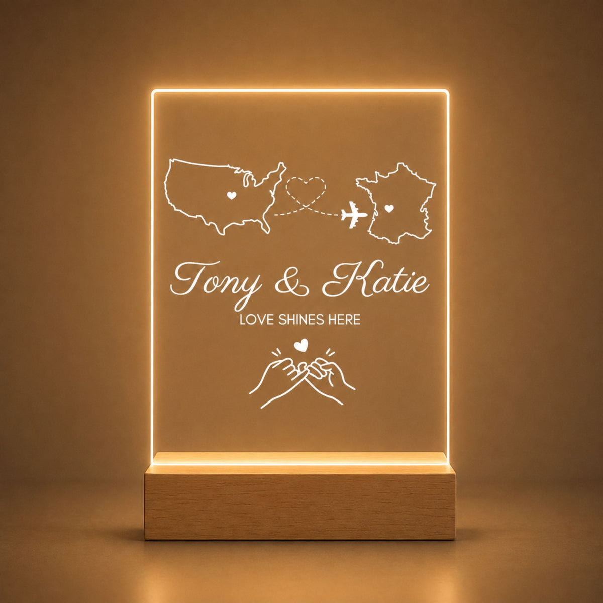 Studio front view of illuminated international map acrylic night light with pinky promise line art glowing warm white on a natural wooden LED base.