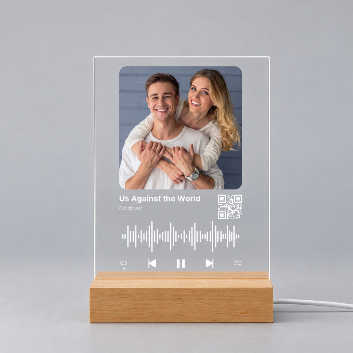 Studio front view of unlit clear acrylic plaque featuring custom photo, song title, sound wave, and scannable QR code on a wooden base.