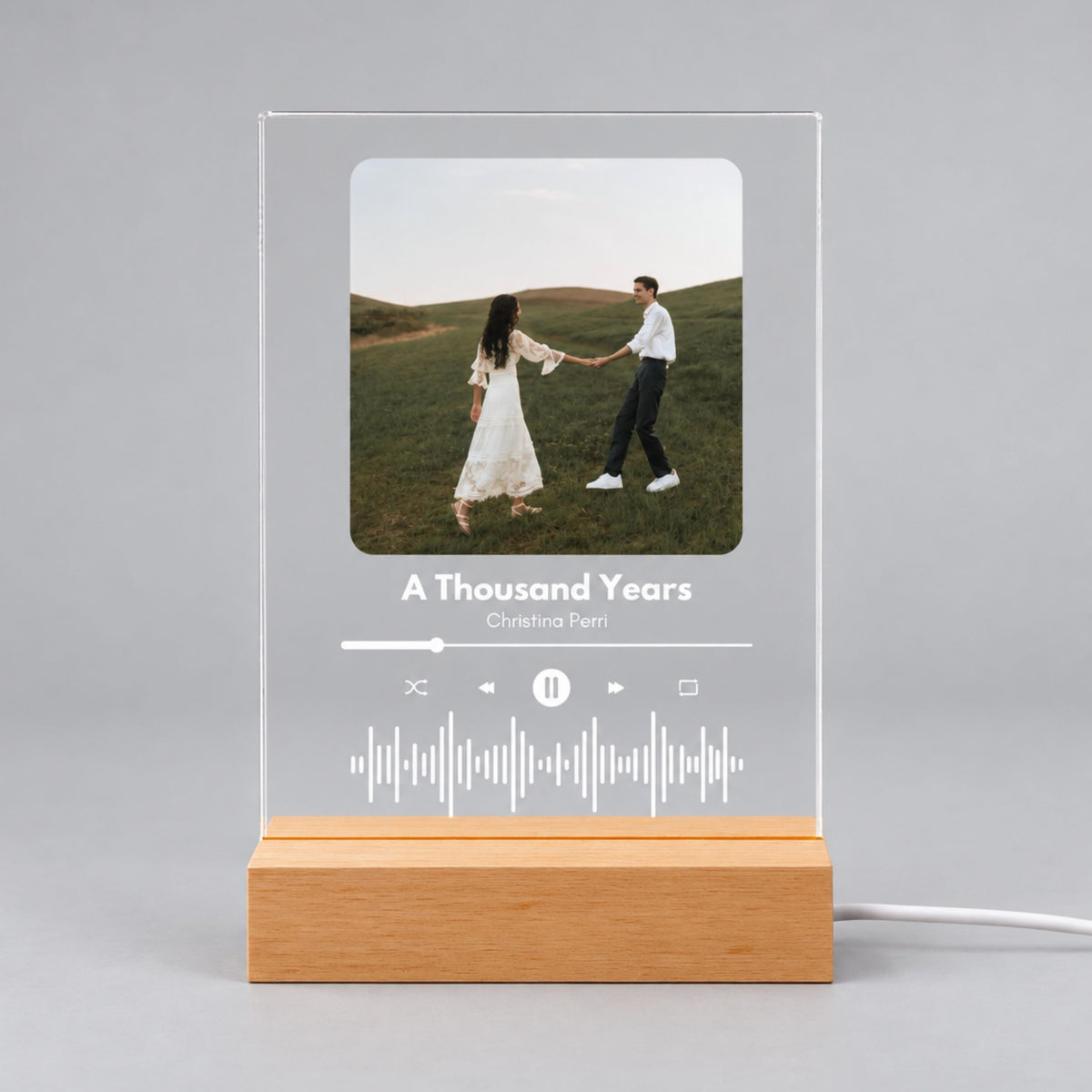 Studio front view of unlit clear acrylic plaque featuring custom couple photo, song title, artist, and sound wave on a wooden base.